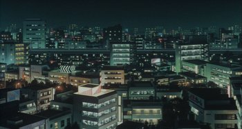 Movie still from “Perfect Blue” (1997), directed by Kô Matsuo – An aerial view of a city at night with buildings lit up at night; Extreme Wide shot, High angle