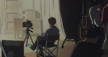 Movie still from “Perfect Blue” (1997), directed by Kô Matsuo – A man sitting in a chair in front of a video camera; Wide shot, High angle