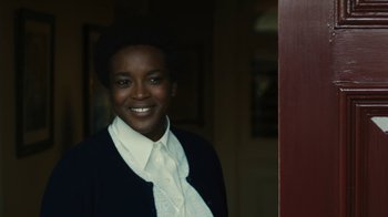 Movie still from “Philomena” (2013), directed by Stephen Frears – A young woman smiling for the camera in front of a door; Close Up shot, Over the shoulder angle