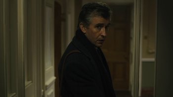 Movie still from “Philomena” (2013), directed by Stephen Frears – A man standing in a hallway wearing a black coat; Close Up shot, Over the shoulder angle