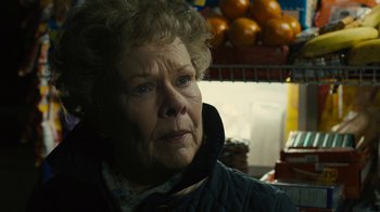Movie still from “Philomena” (2013), directed by Stephen Frears – An older woman in a black jacket is in front of oranges; Close Up shot, Over the shoulder angle