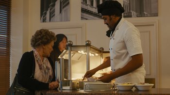 Movie still from “Philomena” (2013), directed by Stephen Frears – A man in a chef's hat is serving food to two women; Medium shot, Over the shoulder angle