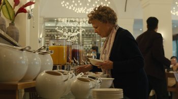 Movie still from “Philomena” (2013), directed by Stephen Frears – A woman in black jacket standing in front of a buffet line; Medium shot, Low angle