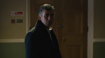 Movie still from “Philomena” (2013), directed by Stephen Frears – A man standing in front of a wooden door; Medium shot, Over the shoulder angle