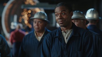 Movie still from “A League of Their Own” (2022), created by Abbi Jacobson – A man in blue jacket standing next to another man in silver hat; Close Up shot, Over the shoulder angle