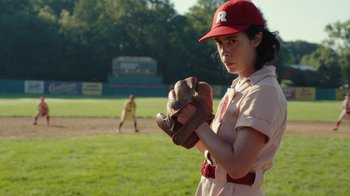 Movie still from “A League of Their Own” (2022), created by Abbi Jacobson – A girl in a baseball uniform holding a baseball glove; Medium shot, Over the shoulder angle