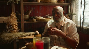 Movie still from “Full Circle” (2023), directed by Steven Soderbergh – An older man sitting at a table in front of a candle; Medium shot, Over the shoulder angle