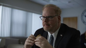 Movie still from “Full Circle” (2023), directed by Steven Soderbergh – A man in a suit and tie eating a sandwich; Close Up shot, Over the shoulder angle