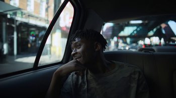 Movie still from “Full Circle” (2023), directed by Steven Soderbergh – A man sitting in the back seat of a car looking out the window; Close Up shot, Over the shoulder angle