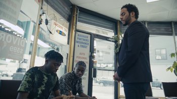 Movie still from “Full Circle” (2023), directed by Steven Soderbergh – A group of men standing next to each other in front of a building; Medium shot, Over the shoulder angle