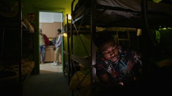 Movie still from “Full Circle” (2023), directed by Steven Soderbergh – A young boy laying on top of a bunk bed; Medium shot, Overhead angle