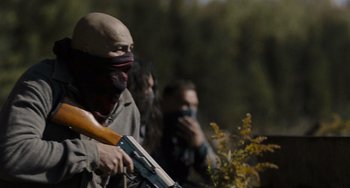 Movie still from “Night Raiders” (2021), directed by Danis Goulet – A man with a mask on holding a rifle; Medium shot, Over the shoulder angle