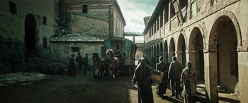 Movie still from “Pinocchio” (2019), directed by Matteo Garrone – A group of men standing around horses in a courtyard; Extreme Wide shot, Low angle