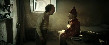 Movie still from “Pinocchio” (2019), directed by Matteo Garrone – A man standing next to another man sitting on a bench; Medium shot, Over the shoulder angle
