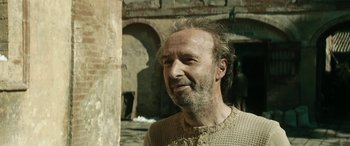 Movie still from “Pinocchio” (2019), directed by Matteo Garrone – A man with a long beard is standing in front of a building; Close Up shot, Over the shoulder angle