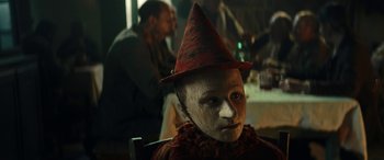 Movie still from “Pinocchio” (2019), directed by Matteo Garrone – A person wearing a red hat and a white mask; Close Up shot, Low angle