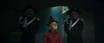 Movie still from “Pinocchio” (2019), directed by Matteo Garrone – A man in a red jacket and a red hat; Medium shot, High angle