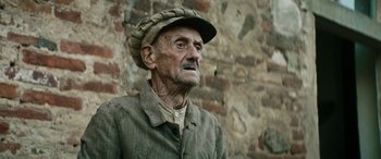 Movie still from “Pinocchio” (2019), directed by Matteo Garrone – An old man wearing a hat standing in front of a brick wall; Close Up shot, Low angle