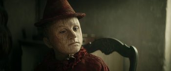 Movie still from “Pinocchio” (2019), directed by Matteo Garrone – A person in a costume with a bat on the back of a chair; Close Up shot, Low angle
