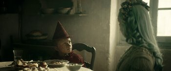 Movie still from “Pinocchio” (2019), directed by Matteo Garrone – A person sitting at a table with a bowl of food; Close Up shot, Over the shoulder angle