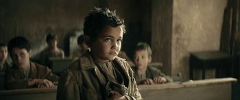 Movie still from “Pinocchio” (2019), directed by Matteo Garrone – A young boy is looking at the camera while sitting in front of another boy; Close Up shot, Over the shoulder angle