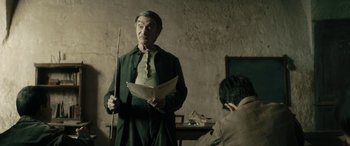 Movie still from “Pinocchio” (2019), directed by Matteo Garrone – An older man holding a stick and a book; Medium shot, Over the shoulder angle