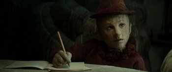 Movie still from “Pinocchio” (2019), directed by Matteo Garrone – A person wearing a mask writing on a piece of paper with a pencil; Close Up shot, Low angle