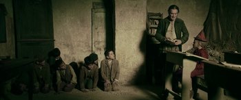 Movie still from “Pinocchio” (2019), directed by Matteo Garrone – A group of young men sitting on the ground in a room; Wide shot, Low angle