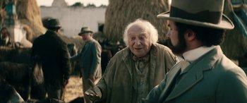 Movie still from “Pinocchio” (2019), directed by Matteo Garrone – An old man with a white beard standing next to a woman; Medium shot, Over the shoulder angle