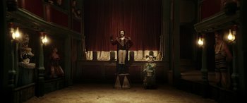 Movie still from “Pinocchio” (2019), directed by Matteo Garrone – A man standing on top of a stool in front of a man sitting on a chair; Wide shot, Low angle