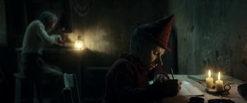 Movie still from “Pinocchio” (2019), directed by Matteo Garrone – An old man wearing a red hat writing on a piece of paper; Medium shot, Low angle