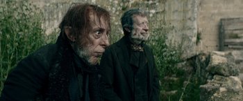 Movie still from “Pinocchio” (2019), directed by Matteo Garrone – Two old men in black suits standing next to each other; Close Up shot, Low angle