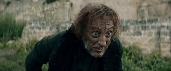 Movie still from “Pinocchio” (2019), directed by Matteo Garrone – An old man with a shaggy beard and long hair looking at the camera; Close Up shot, Low angle