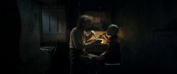 Movie still from “Pinocchio” (2019), directed by Matteo Garrone – An older man and a young boy sitting in a room; Medium shot, Over the shoulder angle