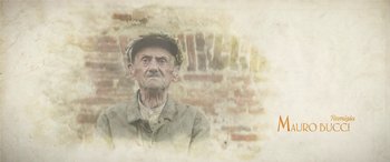 Movie still from “Pinocchio” (2019), directed by Matteo Garrone – An old man wearing a hat standing in front of a brick wall; Close Up shot, Low angle