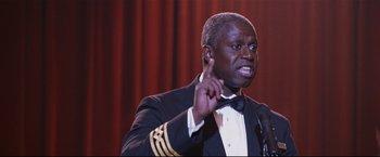 Movie still from “Poseidon” (2006), directed by Wolfgang Petersen – A man in a suit and bow tie speaking at a podium; Close Up shot, Low angle