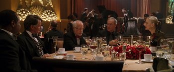 Movie still from “Poseidon” (2006), directed by Wolfgang Petersen – Two men are sitting at a table with wine glasses; Medium shot, Over the shoulder angle