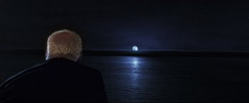 Movie still from “Poseidon” (2006), directed by Wolfgang Petersen – A man looking out at the moon over the ocean; Medium shot, Over the shoulder angle