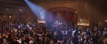Movie still from “Poseidon” (2006), directed by Wolfgang Petersen – A crowd of people in a room with a stage in the background; Extreme Wide shot, High angle