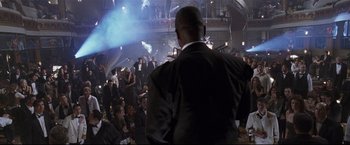 Movie still from “Poseidon” (2006), directed by Wolfgang Petersen – A man in a suit and tie standing in front of an audience; Wide shot, Low angle