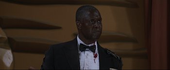 Movie still from “Poseidon” (2006), directed by Wolfgang Petersen – A man in a suit and bow tie with blood on his face; Medium shot, Low angle