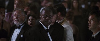 Movie still from “Poseidon” (2006), directed by Wolfgang Petersen – A man wearing a suit and tie standing in a crowd; Close Up shot, Over the shoulder angle
