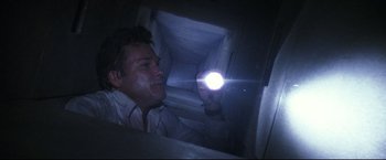 Movie still from “Poseidon” (2006), directed by Wolfgang Petersen – A man holding up a flashlight while looking into a spiral staircase; Medium shot, Overhead angle