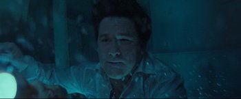 Movie still from “Poseidon” (2006), directed by Wolfgang Petersen – A man in a white shirt is sitting in a dark room; Close Up shot, Overhead angle