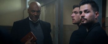 Movie still from “Prey for the Devil” (2022), directed by Daniel Stamm – Two men are standing next to each other in a room; Medium shot, Low angle