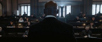 Movie still from “Prey for the Devil” (2022), directed by Daniel Stamm – A man in a black suit is in a courtroom; Medium shot, Over the shoulder angle
