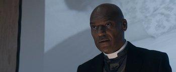Movie still from “Prey for the Devil” (2022), directed by Daniel Stamm – A man in a priest's outfit stares at the camera; Close Up shot, Low angle