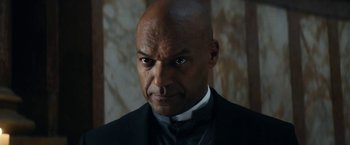 Movie still from “Prey for the Devil” (2022), directed by Daniel Stamm – A man in a suit and tie looking at the camera; Close Up shot, Low angle