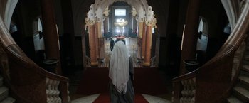Movie still from “Prey for the Devil” (2022), directed by Daniel Stamm – A woman wearing a veil standing in front of an archway; Wide shot, Low angle