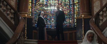 Movie still from “Prey for the Devil” (2022), directed by Daniel Stamm – A man and a woman standing in front of a stained - glass window; Wide shot, Low angle